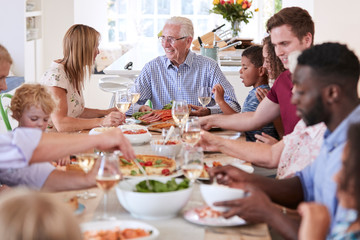 Group Of Multi-Generation Family And Friends Sitting Around Table And Enjoying Meal