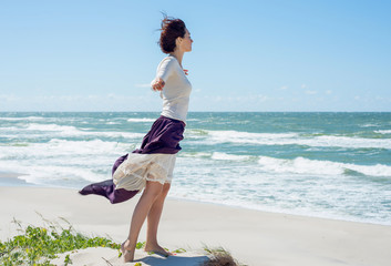 Young brunette woman in dress stands on the hill by the sea