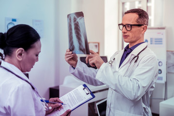 Competent Asian doctor filling form during research