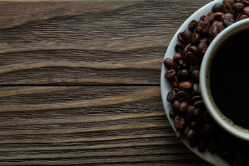 Cup of coffee, coffee beans on saucer on wooden background. Selective focus