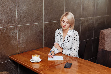 Blonde woman in cafe writing in notebook