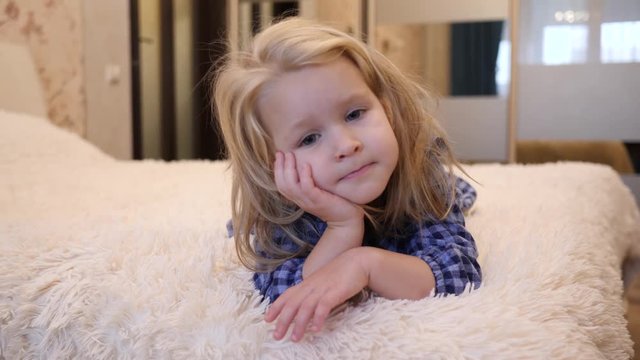 Dreamly cute little child girl lying on a sofa white rug watching camera