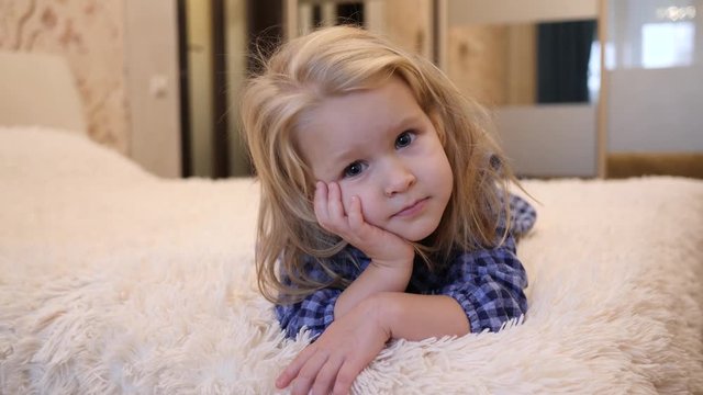 Dreamly cute little child girl lying on a sofa white rug watching camera