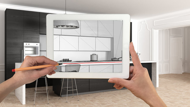 Hands holding and drawing on tablet showing modern kitchen in classic apartment interior sketch. Real finished minimalist interior in the background, architecture design presentation