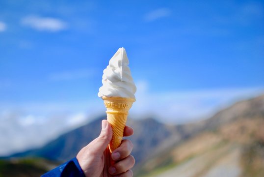 Milky vanilla ice cream in the waffle cone is hold in the hand with background of clear blue sky and mountain