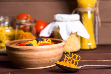 Good food is lined with pasta on a spoon near a plate with ready-made pasta with tomato, basil and parmesan on a wooden rural table. Healthy Vegan Nutrition Concept