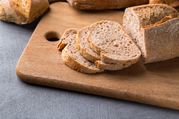 Freshly baked sliced bread on wooden cutting board on the grey stone table, close up.