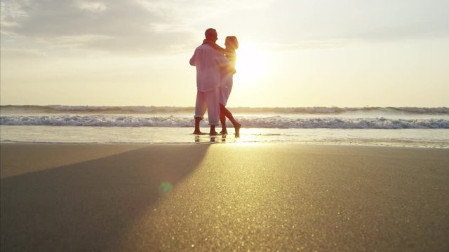 Silhouette of mature Caucasian couple dancing on the beach at sunset