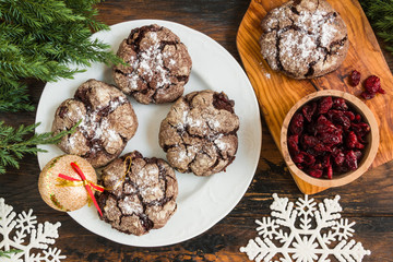Cracked chocolate cookies with cranberries on white plate on wooden rustic table. Christmas decoration, top view, close-up