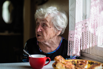 Retired elderly woman in the kitchen of his house sitting at the table.