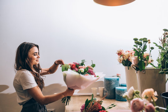 Young Smiling Brunette Female Business Woman Florist Creating Beautiful Bouquet Of Colorful Different Flowers In Modern Interior Floral Shop. Side View