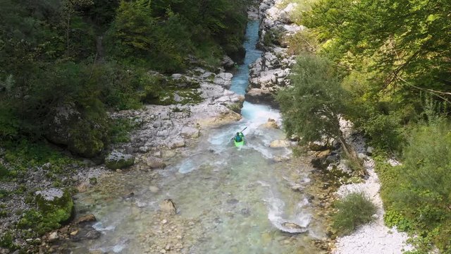 Person kayaking down small river rapids that carve through the forest.