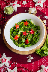 Spinach avocado fresh salad with Christmas red stars. Christmas food on red teblecloth