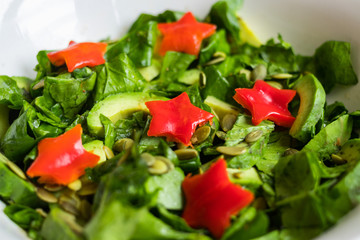 Spinach avocado fresh salad with Christmas red stars. Christmas food on red teblecloth