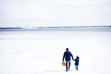 Fototapeta na wymiar Father with daughter walking near frozen river with snow around