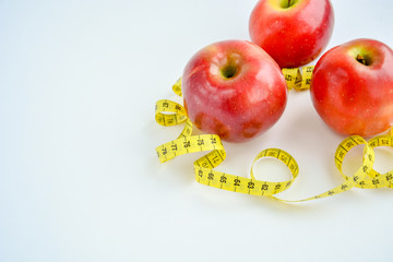 Red juicy apples are on a white background, there is a bright yellow measuring tape around the apples.