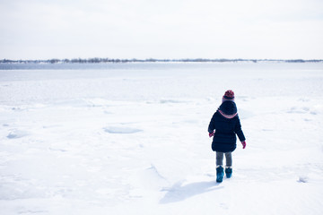 Fototapeta na wymiar Little girl walking on the frozen river with snow aroung