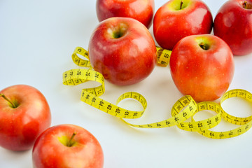 Red juicy apples are on a white background, there is a bright yellow measuring tape around the apples.