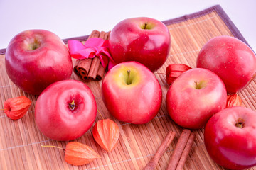 Red apples lie on a wooden background in the company of cinnamon and Physalis