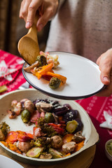 Woman hands take, put, mix with spatula baked, roasted, grilled vegetables. Beetroot, carrot, mushrooms, pumpkin, brussels sprouts with avocado dip sauce. Christmas lunch or dinner. Red tablecloth