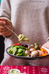 Woman hand adds sauce to baked, roasted, grilled vegetables. Beetroot, carrot, mushrooms, pumpkin, brussels sprouts with avocado dip sauce. Vegan lunch, vegetarian dinner