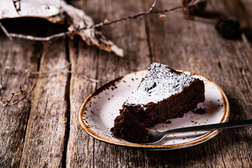 Kladdkaka. Traditional Swedish moist chocolate cake on old rustic wooden table decorated dry twigs,...