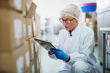 Female worker crouching and using tablet for stock control.