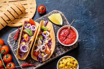 Fototapeta na wymiar Tacos with chicken, vegetables and salsa sauce in tartilla on dark background