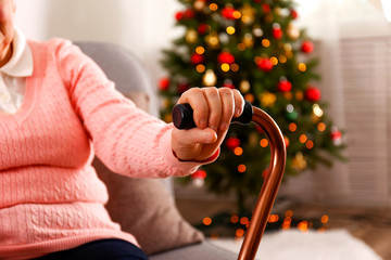 Elderly woman celebrating Christmas at home, with decorated holiday pine tree on background. Old...