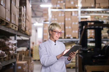 Happy Caucasian factory worker using tablet while standing in warehouse.