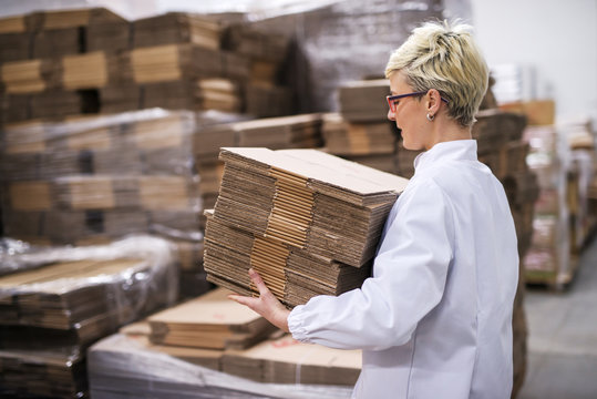 Woman carrying unmade cardboard boxes. Side view, warehouse interior.