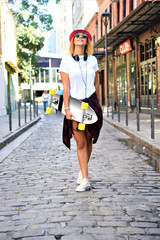 Beautiful hipster girl with skate board wearing sunglasses walking the city streets. Hipster lifestyle