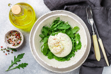 Delicious Creamy Italian Burrata Cheese Served with Olive Oil, fresh arugula and spices in a white plate © la_vanda