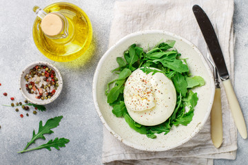 Delicious Creamy Italian Burrata Cheese Served with Olive Oil, fresh arugula and spices in a white plate