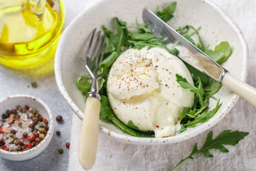 Delicious Creamy Italian Burrata Cheese Served with Olive Oil, fresh arugula and spices in a white plate