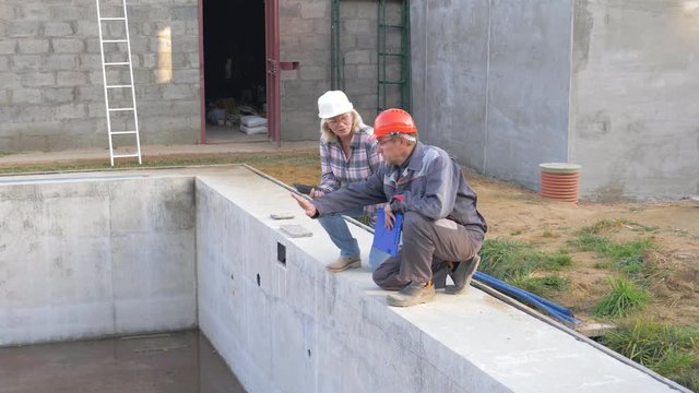 Construction Workers In A Helmet And Discuss Building Houses With A Pool