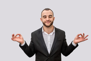 Calm and peaceful young man in suit meditating. He keeps eyes closed. His hands are aside of body. Isolated on white background.