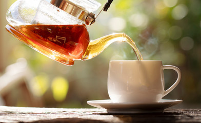 Hot tea pouring from tea pot on nature background