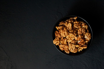 Walnut in a bowl on a black slate or stone background - healthy snack.Top view with copy space.