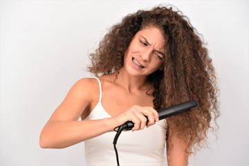 Curly hair. Beauty Close-up of brunette girl with blowing hairstyle holding straightening iron....