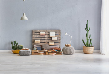 Fototapeta na wymiar Pallet headboard bed and book style, grey puff vase of cactus and white lamp.
