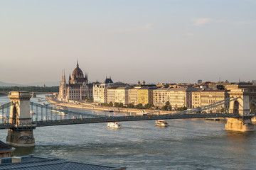 Panoramic view from the Castle hill in Budapest during sunset of the Hungarian Parliament building, the Chain Bridge of the Danube with cruise ships and the buildings on the river bank. 