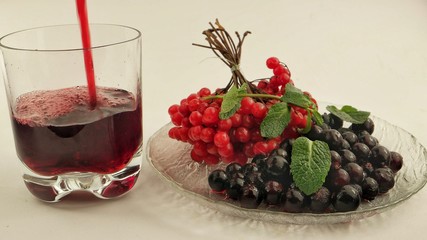 A glass of berry juice and a plate of black currant and viburnum on a white background