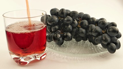A glass of black grape juice and a plate with grapes on a white background