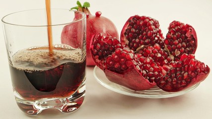 A glass of pomegranate juice and a plate with pomegranate on a white background