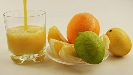 A glass of citrus juice and a plate with orange, lemon and lime on a white background