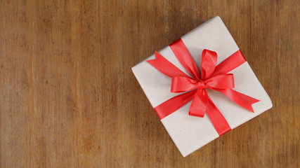 Gift box wrapped in brown recycled paper with red ribbon bow top view on wood background