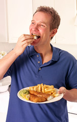 MAN IN KITCHEN EATING FISHING AND CHIPS