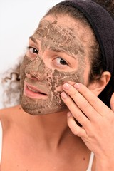Woman removing facial dried clay mud mask in front of mirror. Skin care. Girl taking care of her complexion. Beauty spa treatment.