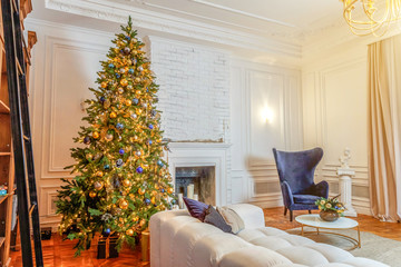 Classic Christmas decorated interior room New year tree. Christmas tree with gold decorations. Modern white classical style interior design apartment with fireplace and armchair. Christmas eve at home